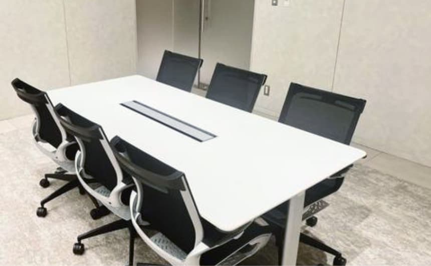 白い会議テーブルと黒いオフィスチェアが配置された会議室